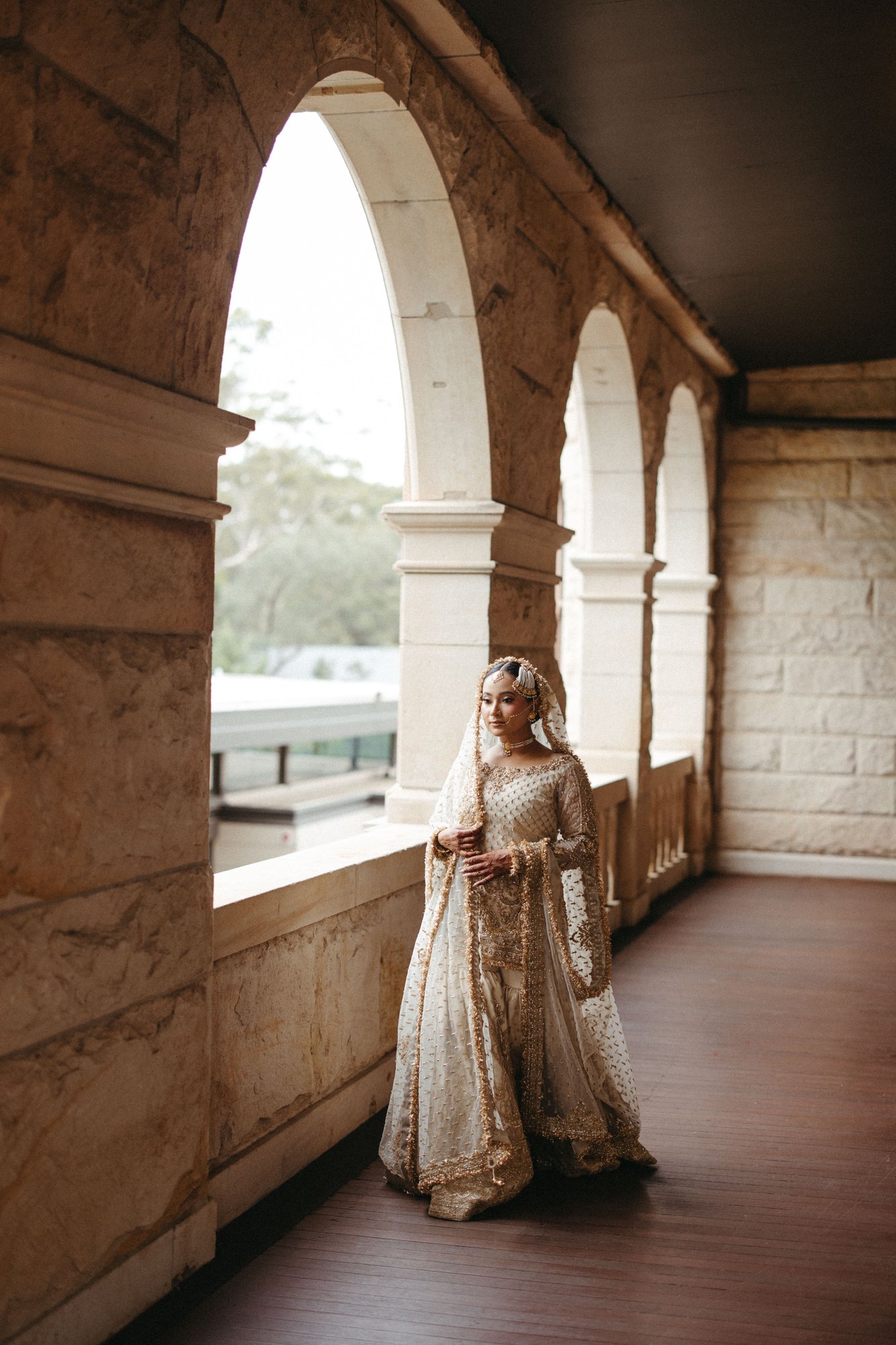 A bride beneath sunlit stone arches